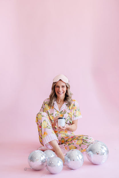 woman in pajamas wearing sleep mask holding mac + mitchell nightcap magnesium cream, pink background