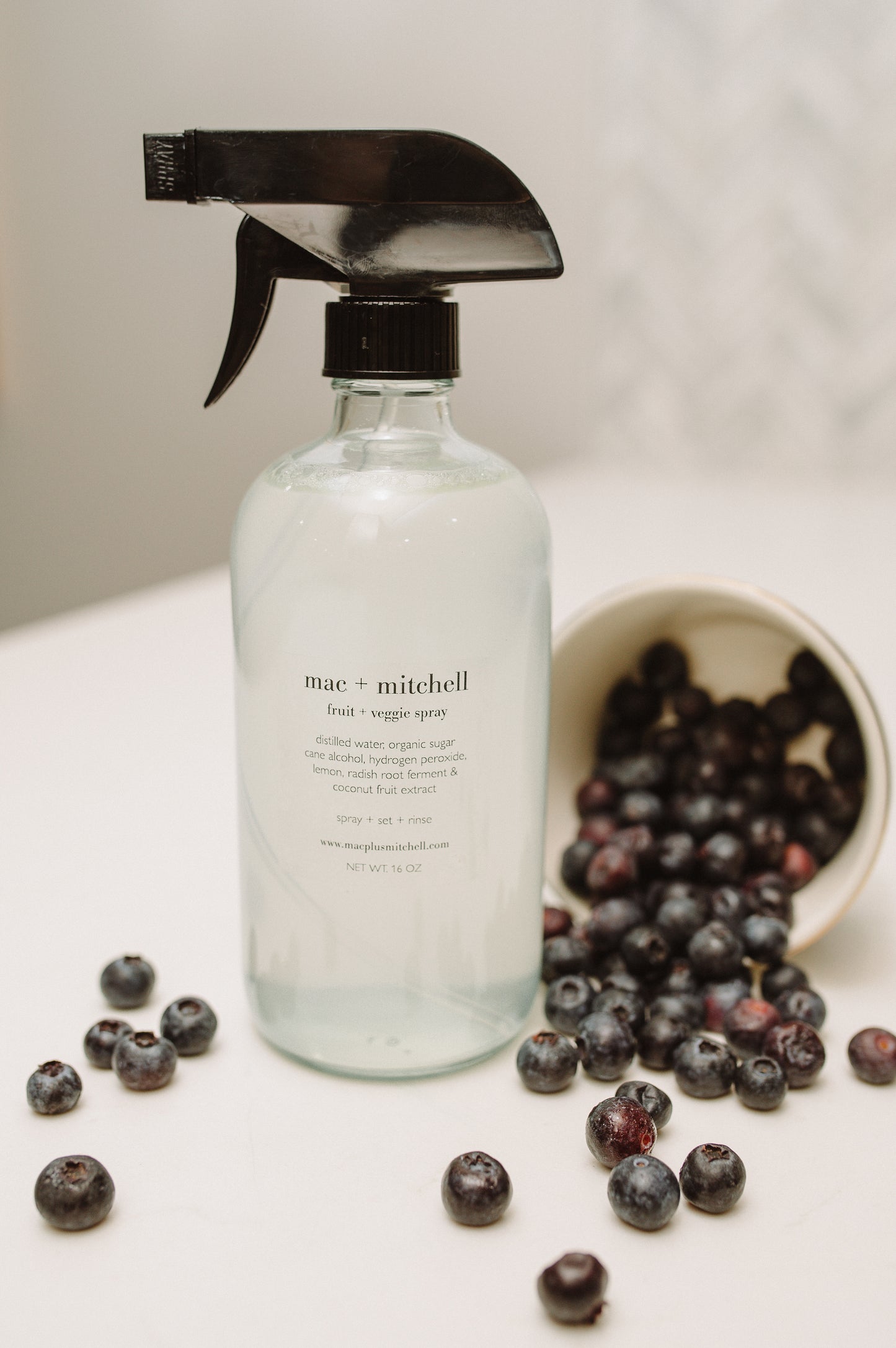Fruit and veggie wash spray bottle with bowl of blueberries, a plant-based cleaner with lemon oil and hydrogen peroxide to extend produce life
